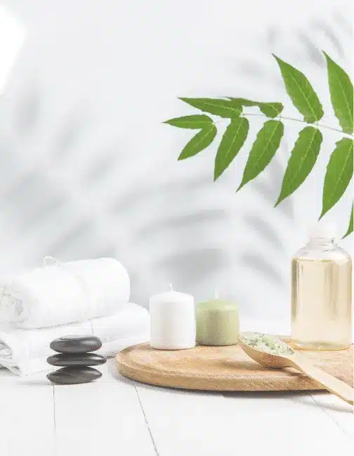 Rolled white towels, candles, massage stones and a bottle of oil on a wooden tray